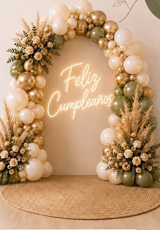 Arco orgánico con globos en tonos neutros y verdes, letrero neón «Feliz Cumpleaños», rosas, pampas y follaje.